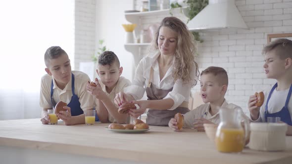 Attractive Happy Woman and Her Four Teen Sons Eating Pies and Drinking Orange Juice in the Kitcken alt