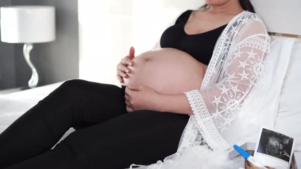 female hands pat the pregnant belly on the bed alt