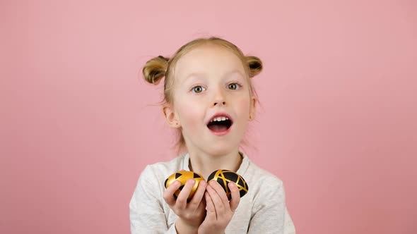 Funny Little Blonde Girl Smiling and Playing with Golden Easter Eggs on Pink Background alt