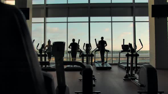 Three Unrecognizable People Running on Treadmills in an Empty Gym alt