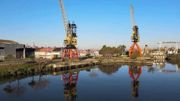 Low backward aerial of port cranes by still water in Buenos Aires alt