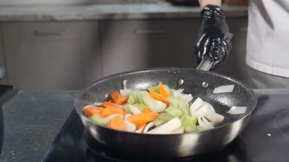 Chef in Black Gloves Cooking Vegetables on Frying Pan in Restaurant Kitchen alt