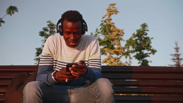 Happy African Man is Walking and Listening to Music By Wireless Headset in City