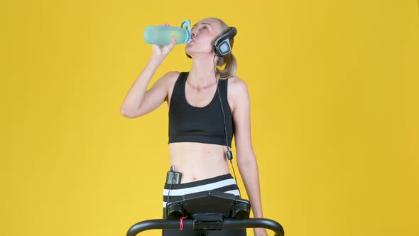 blonde girl works out on a treadmill and drinking water from sport bottle.