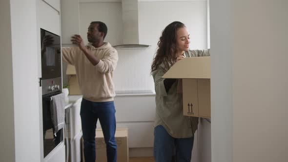 Excited Young Couple In New Home Unpacking Removal Boxes In Kitchen Together