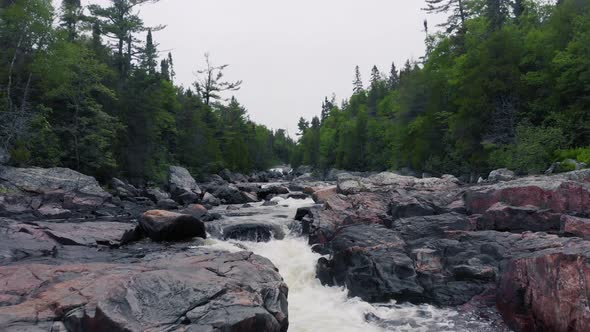 Drone footage flying low slowly over a rushing river with rapids surrounded by forest with boulders alt
