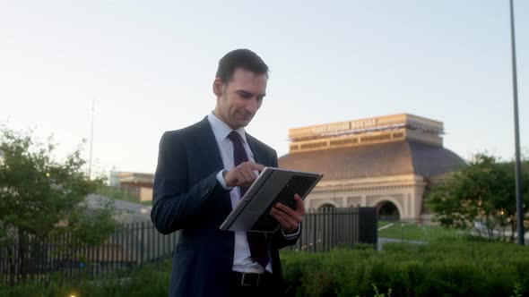 Man in Dark Blue Suit and Tie in Formal Wear Writes or Surfs Something on Tablet PC alt