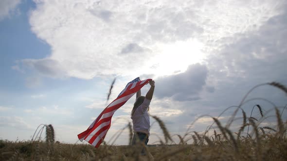 Happy Patriotic Young Woman Waves the US Flag and Jumps Into the Field