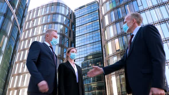 Low Angle Shot Two Businessmen in Medical Mask Meet a Businesswoman Also Wearing a Mask and Shake alt