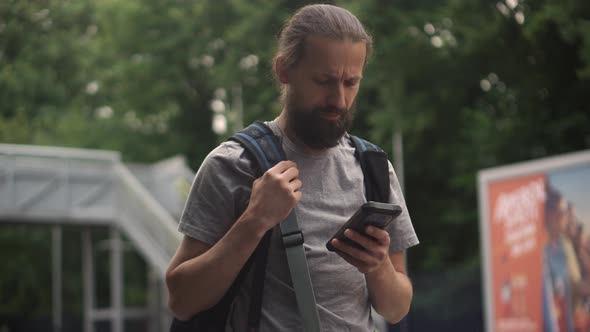 Elegant Man Checking Email on Mobile Phone While Walking with Backpack Waiting for the Train on alt