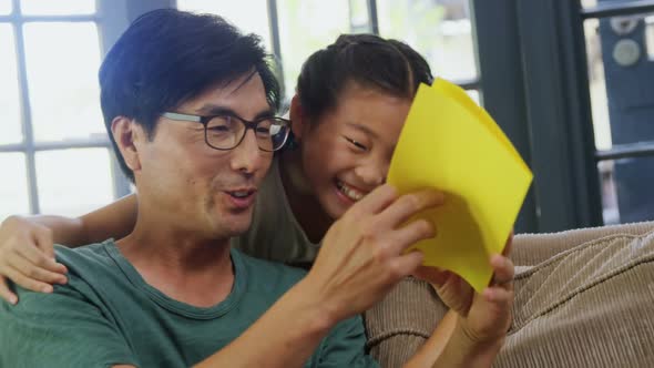 Father and daughter reading greeting card in living room 4k alt
