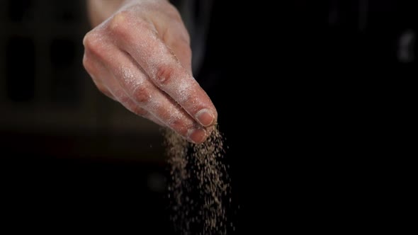 Closeup of a Hand is Sprinkling Spices on a Black Background in Slow Motion