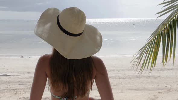 Young woman with bikini and hat on tropical beach looking at the ocean in ultra slow motion camera f alt