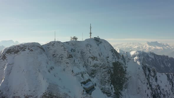 Drone flying towards radio tower on top of snow covered mountain summit and revealing beautiful vall alt