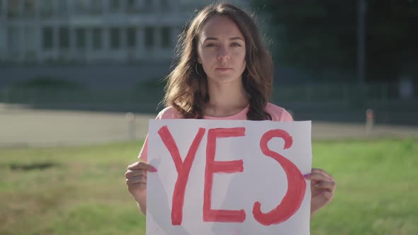 Portrait of Young Brunette Woman Holding Yes Poster Outdoors. Serious Female Caucasian Activist alt
