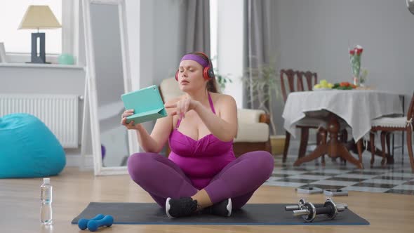 Confident Plussize Caucasian Woman Enjoying Music in Headphones Sitting on Exercise Mat Filming alt