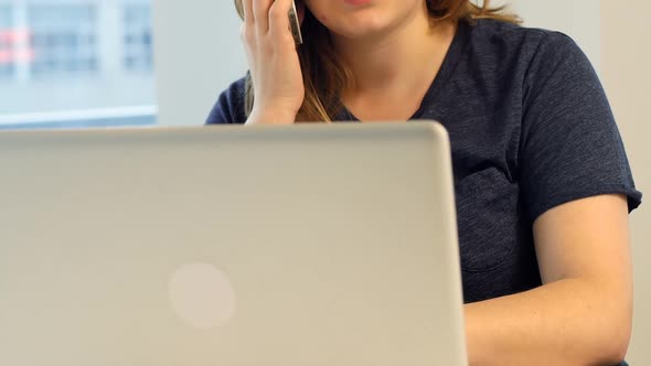 Woman using laptop while talking on mobile phone alt