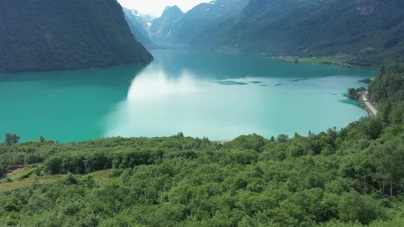 Green lush forest and glacier green freshwater lake in Olden Norway - Aerial flying over forest and alt