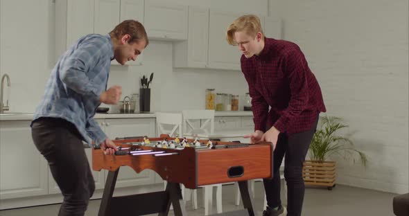 Joyful Guys Playing Foosball in Loft Apartment alt