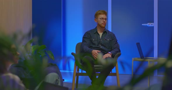 Young Redhaired Man Sits in a Chair and Speaks on a Talk Show