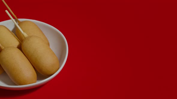 Close Up View of White Plate with Corn Dogs Shotting on Red Background alt