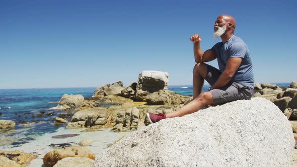Senior african american man exercising sitting on rocks by the sea alt
