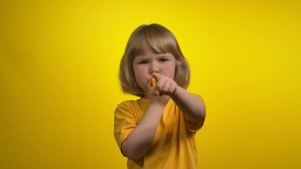 Cute Little Girl with Short Hair is Blowing in a Whistle and Pointing to Camera alt