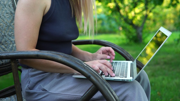Beautiful blonde girl typing on a laptop while sitting in a rocking chair outdoors