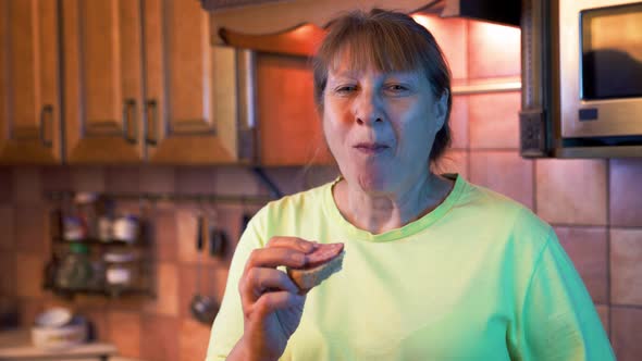 Hungry middle aged woman opens a refrigerator at night and eating hamburger with sausage. alt