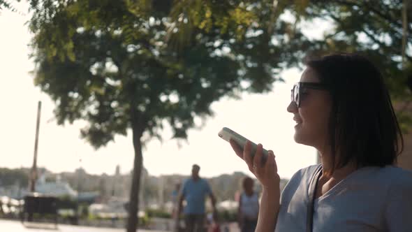 Portrait of a Girl Using the Voice Recognition of the Phone and Looking at Cell Phone Near Hotel on alt