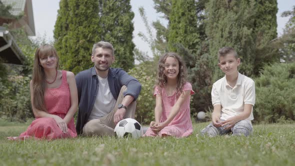 Happy Family Sitting on the Grass in the Garden Together. Mother, Father, Son, and Daughter alt