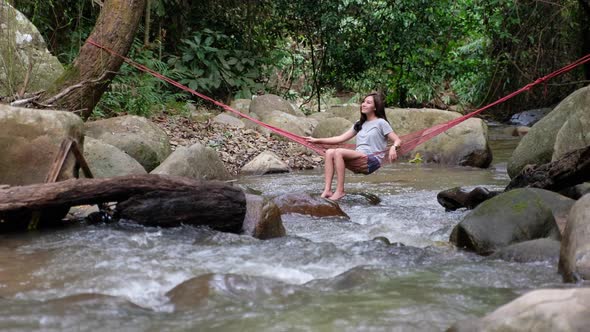 A beautiful young asian woman sitting and relaxing in hammock in waterfall stream