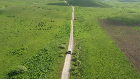 Top view on the driving car of the mountain road through the green field
