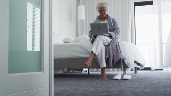 African american senior woman using laptop while sitting on the bed at home alt
