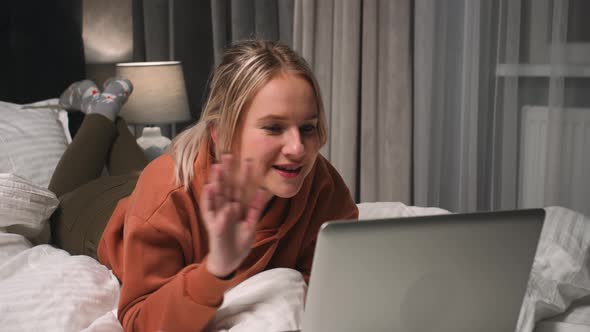 Portrait of Smiling Woman Waving Hands at Laptop Camera in Home Bedroom alt
