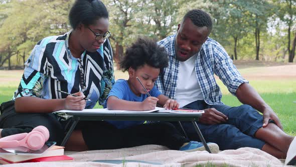 African American parents and child enjoy the picnic in park, and the son made homework