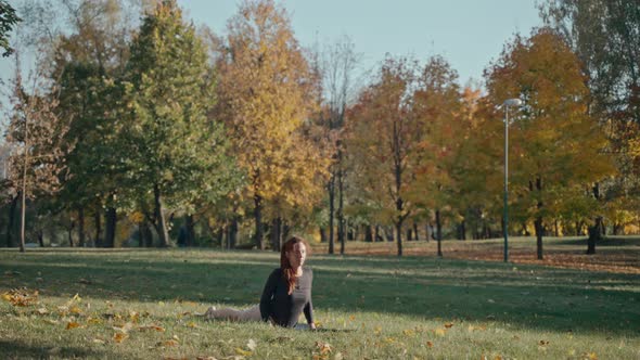 Young Woman Arching Backward in Autumn City Park on a Yoga Mat on a Sunny Day alt