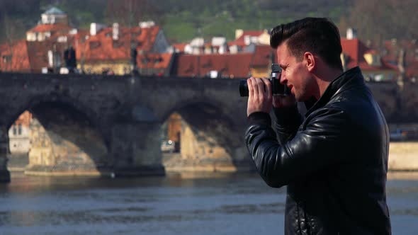 A Young Handsome Man Takes Photos of a Quaint Town with a Camera - a Bridge Over a River alt