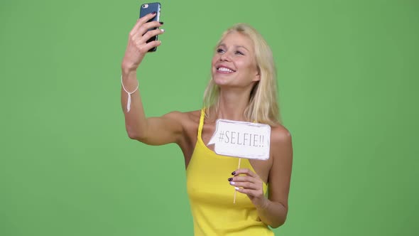 Young Happy Beautiful Blonde Woman Taking Selfie with Paper Sign