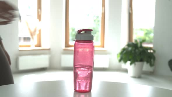 Woman Putting Pink Plastic Bottle of Water on Table in Bright Room Closeup