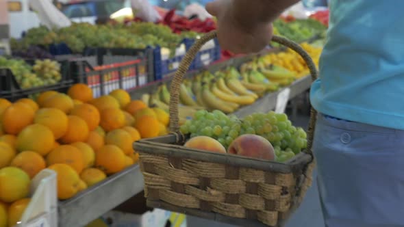 Man with basket of grapes and peaches on fruit market alt