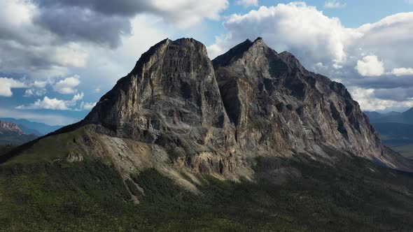 Orbiting aerial shot of famous Sukakpak Mountain against white clouds in summer Alaska without snow alt