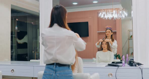 Hairdresser Combing Hair to a Girl in a Beauty Salon in Front of a Large Mirror alt