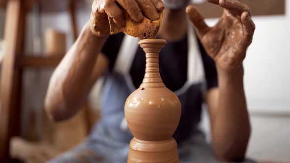 Hands of man at pottery wheel forming clay using sponge alt