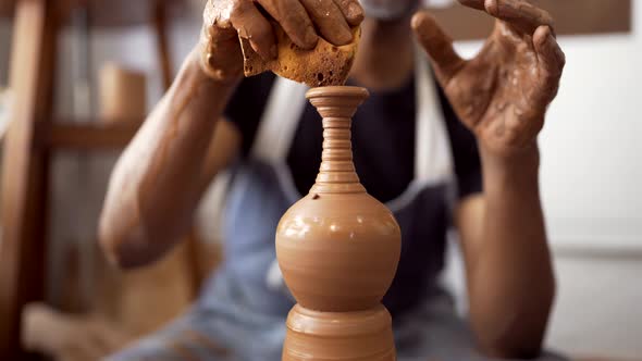 Hands of man at pottery wheel forming clay using sponge