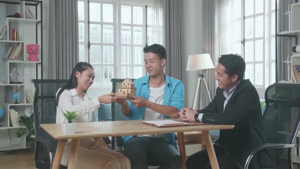 Asian Real Estate Agent With A House Purchase Contract Paper Giving A House Model To A Couple alt