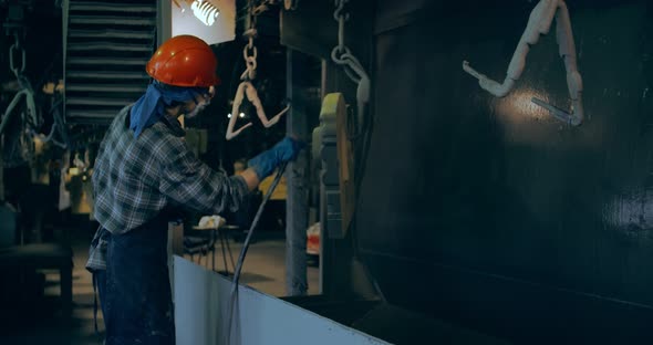 A girl in an orange helmet launches a metal part. At a machine-building plant