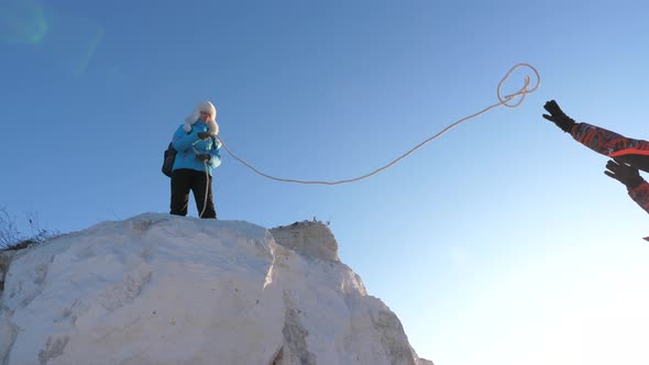 Strong Woman Traveler Helps Man Climber To Climb Mountain on Rope. Teamwork of Tourists. Joyful alt