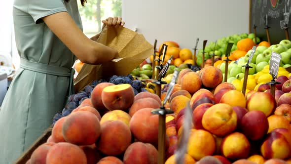 Young Caucasian Woman is Choosing a Peaches at Grocery Store