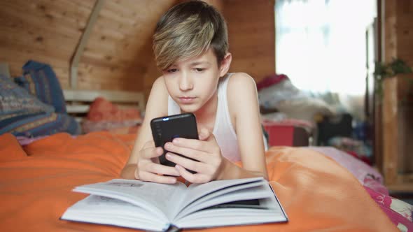 boy lies on the bed pretends to read a book but uses the phone